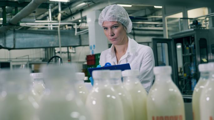 一名女员工正在食品厂检查乳制品生产过程。