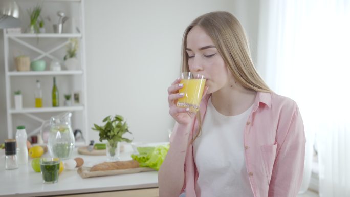 金发碧眼的年轻妇女喝着橙汁，对着镜头微笑