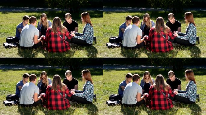 一群大学朋友围坐在绿草上祈祷。