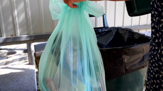 妇女提着垃圾袋，把塑料垃圾袋放进垃圾桶