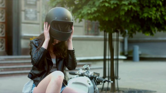 穿着皮夹克的漂亮黑发女性，脱下摩托车头盔