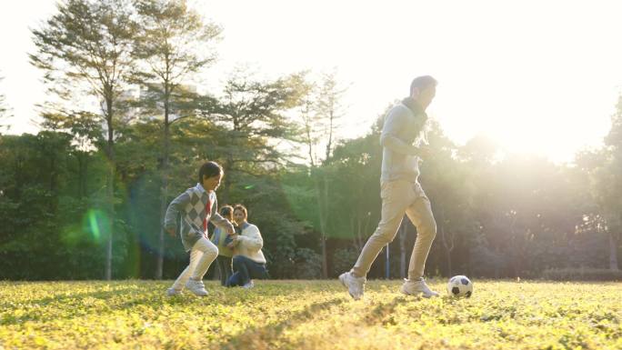 亚洲小男孩和爸爸在公园外面踢足球