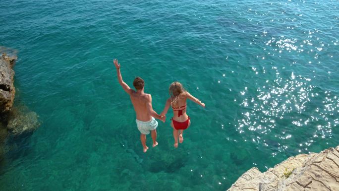 一对年轻夫妇手牵着手从悬崖上跳入大海。