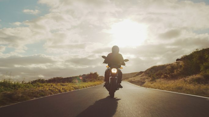 日落时分，摩托车手沿着乡村公路行驶