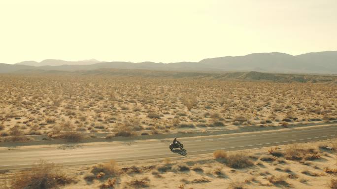 日落时骑摩托车沿沙漠公路行驶的鸟瞰图