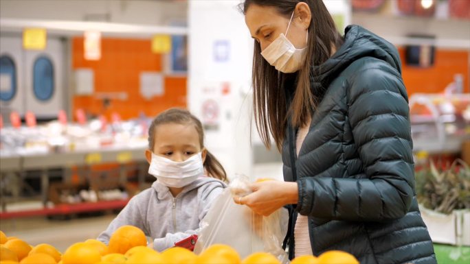 带着戴着医用口罩的妈妈和女儿在超市买橘子