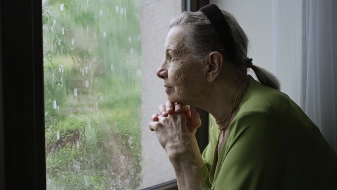 老妇人向窗外望去老人眺望远望窗户窗台雨中