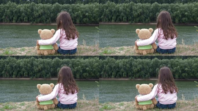 小女孩在河边拥抱一只泰迪熊。