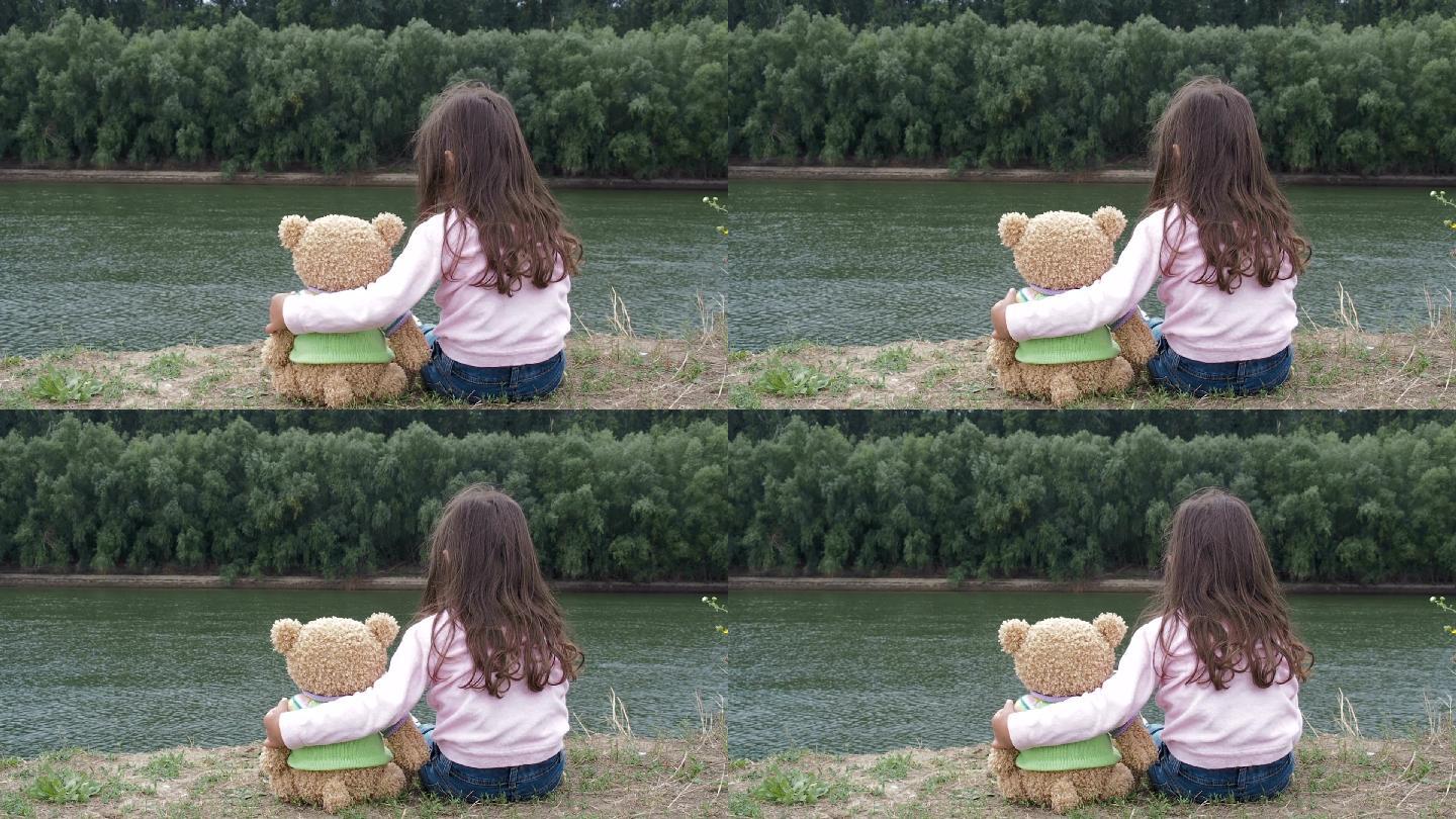 小女孩在河边拥抱一只泰迪熊。