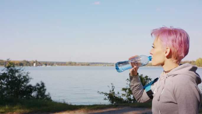 一个粉红色头发的年轻人在湖边慢跑后喝水。