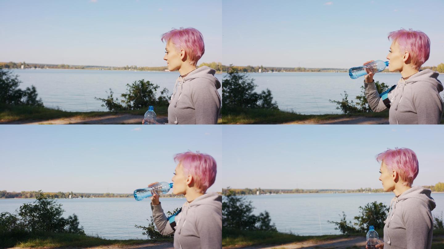 一个粉红色头发的年轻人在湖边慢跑后喝水。