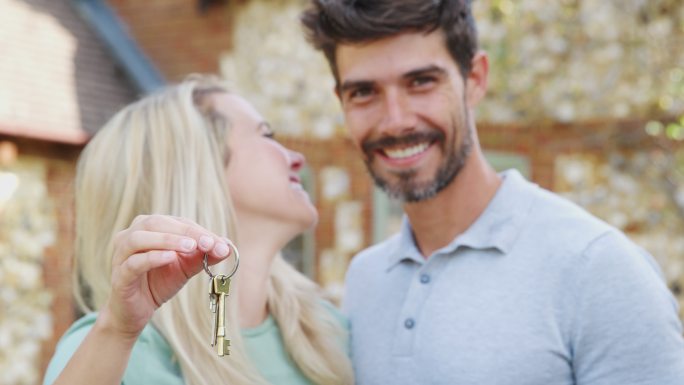 夫妇在新居外拿着房子钥匙的照片