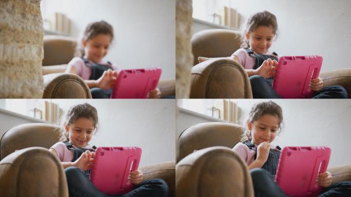 坐在家里扶手椅上玩数字平板电脑的女孩