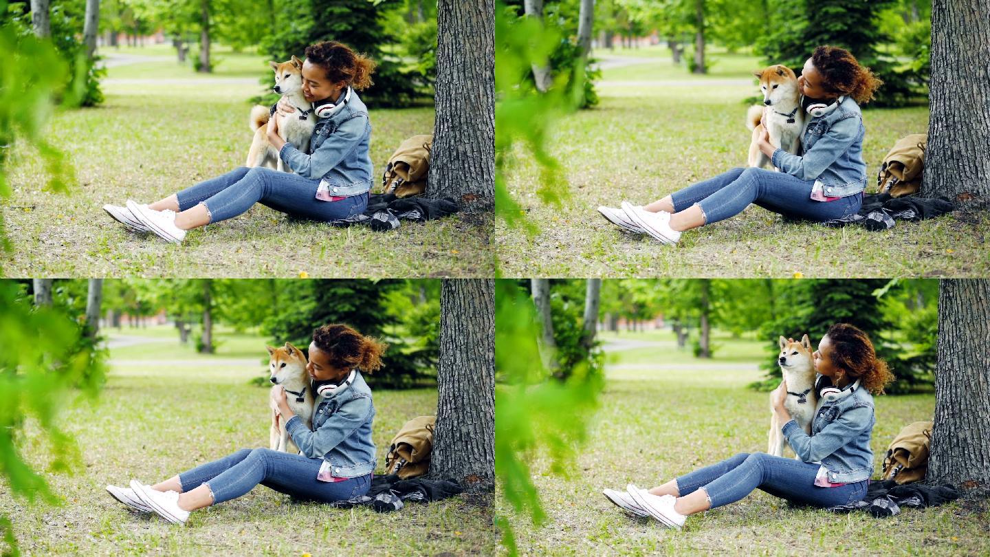 坐在公园绿草上的小女孩和宠物狗玩耍