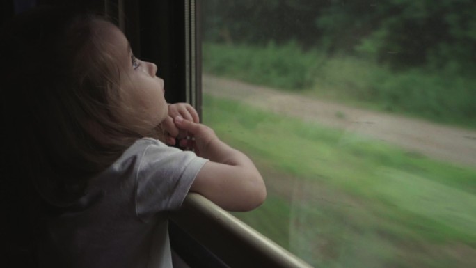 可爱的小女孩从火车窗口向外看的照片。