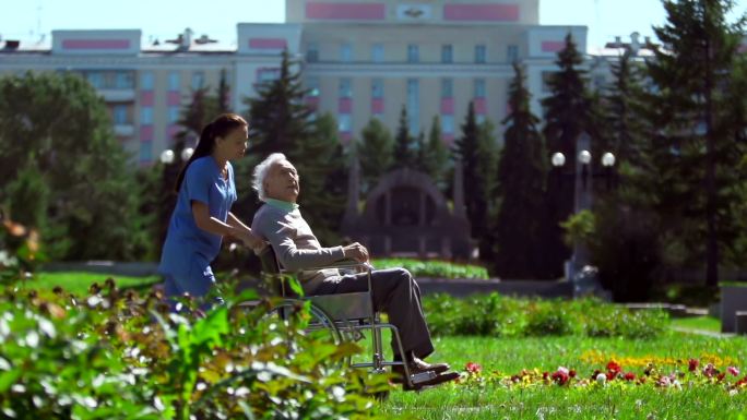 护士带着坐在轮椅上的病人在医院外散步