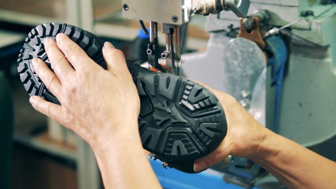工厂工人正在用缝纫机缝制靴子