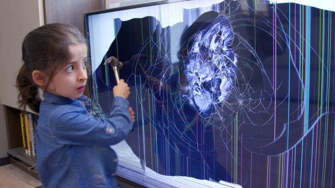 恼怒的女孩用锤子打碎液晶电视屏幕