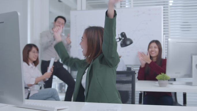 兴奋的女商人坐在办公桌前，举起双臂庆祝成功