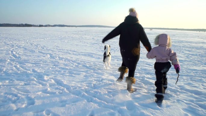 年轻女子带着小女孩和小狗在结冰的湖面奔跑