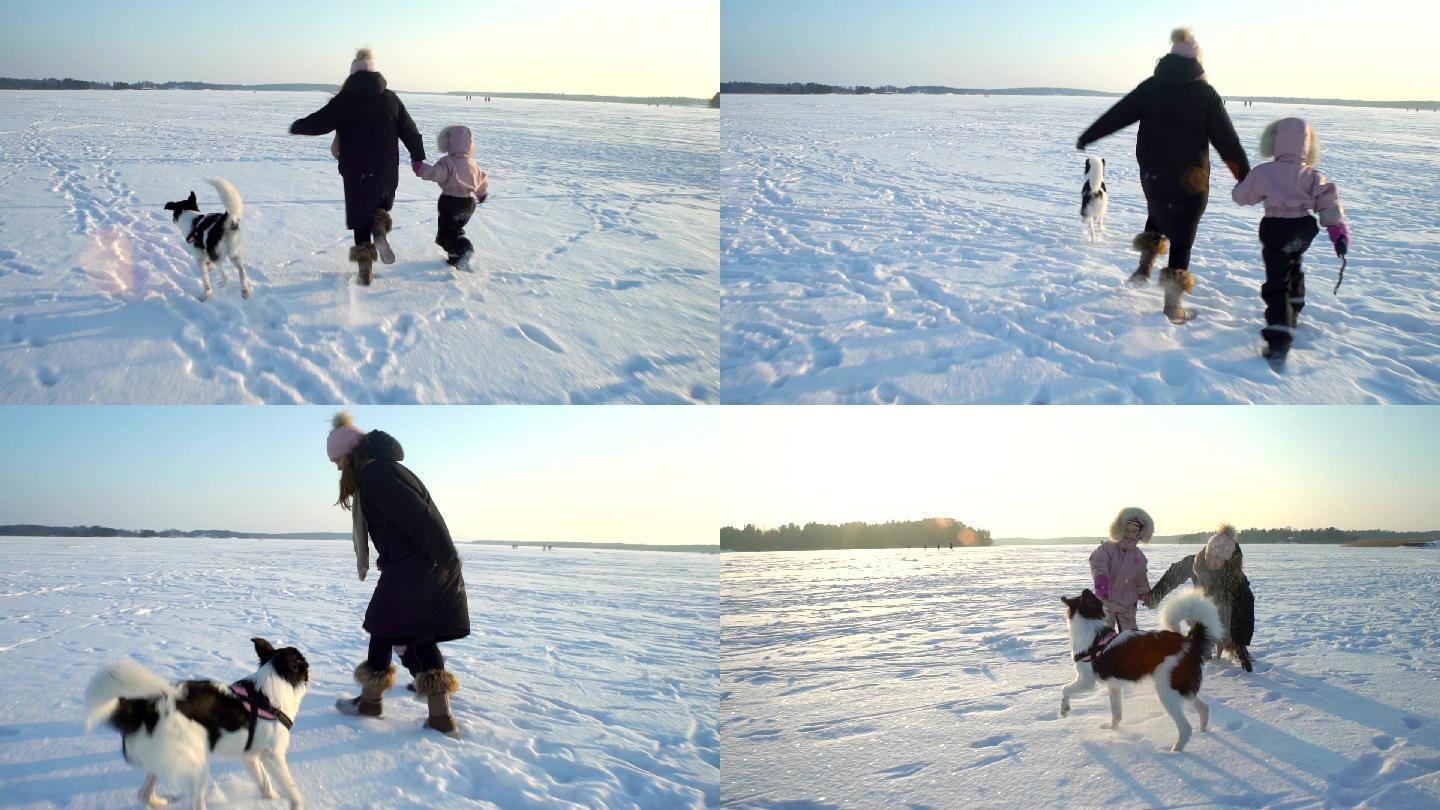 年轻女子带着小女孩和小狗在结冰的湖面奔跑