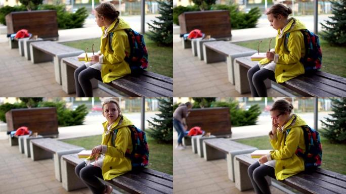 孤独的女孩坐在学校附近的长椅上