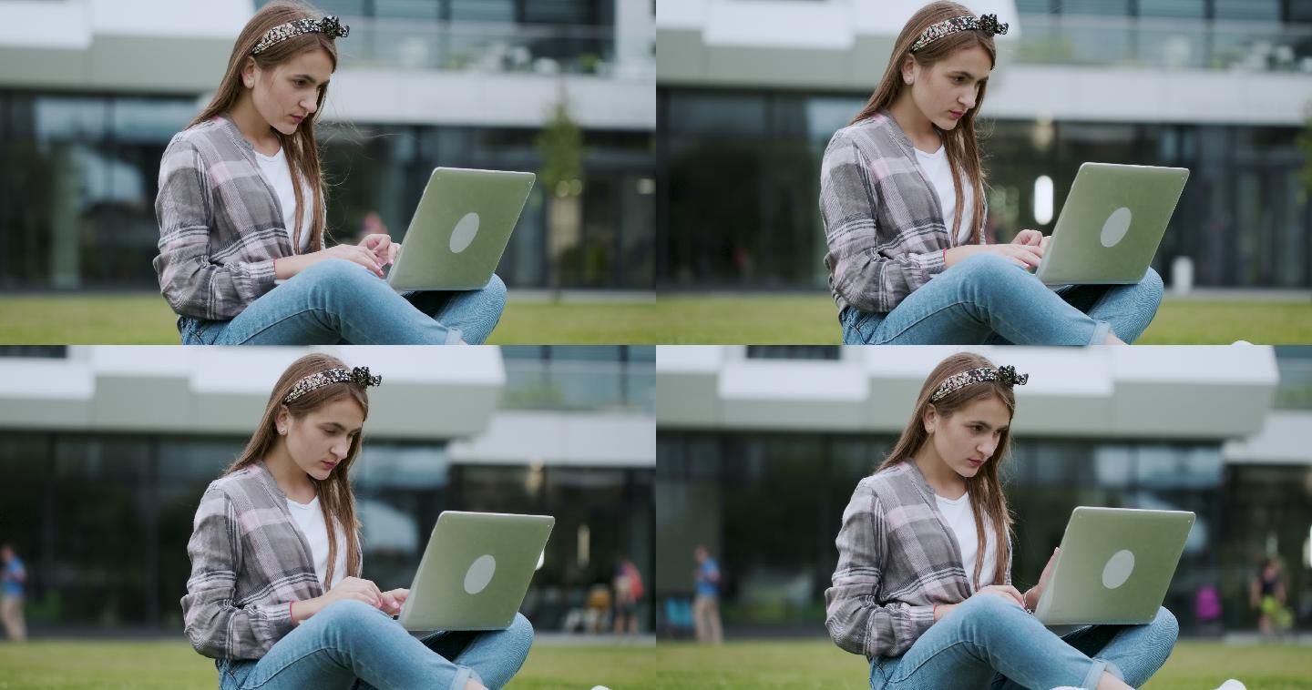 女孩坐在草坪上对着大建筑物在户外用笔记本