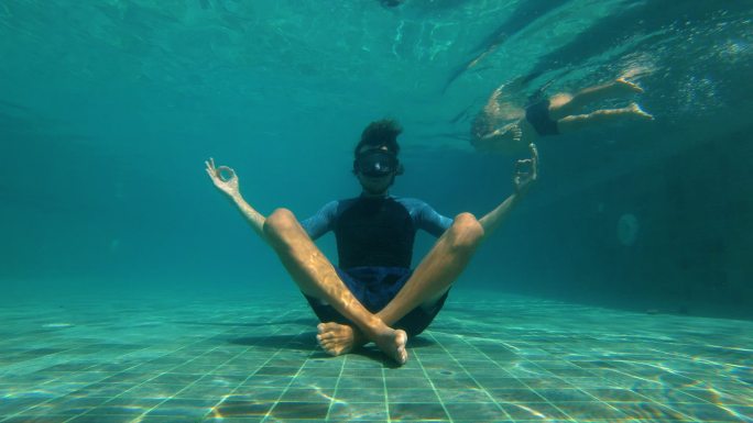 一个年轻人在游泳池底部做瑜伽冥想