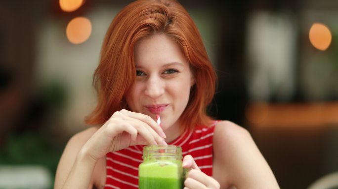 美丽的女孩喝着健康的绿色果汁