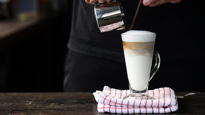 咖啡师将奶油浓缩咖啡倒入牛奶泡沫层