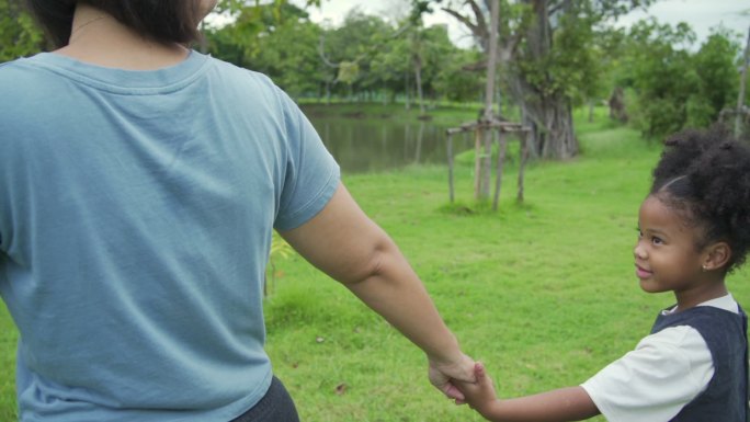 单身母亲和小女儿手牵着手，一起在公园里散
