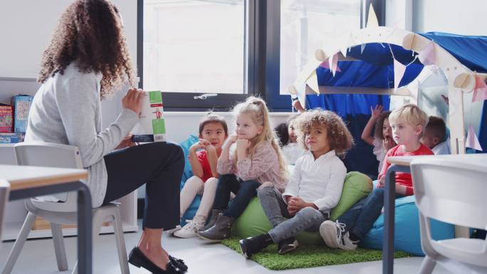 幼师在教室舒适的角落里给孩子们读书