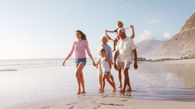 多代人家庭在暑假沿着海滩散步