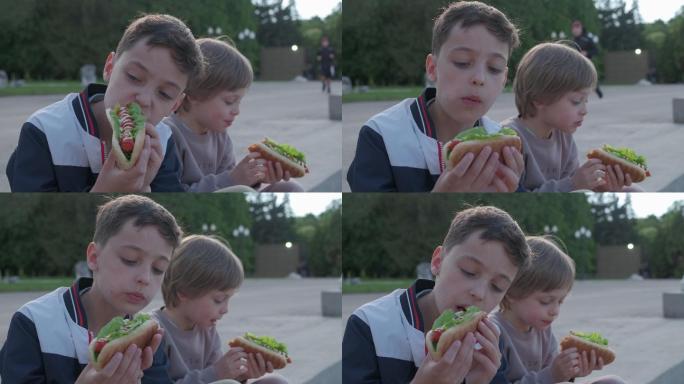 两个小男孩在户外吃热狗。