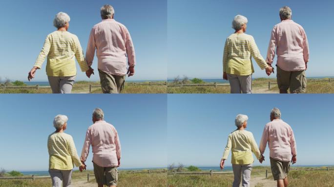 一对老夫妇手牵着手走在通往海滩的小路上