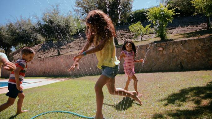 一群孩子在花园的喷水器上玩耍和跳跃