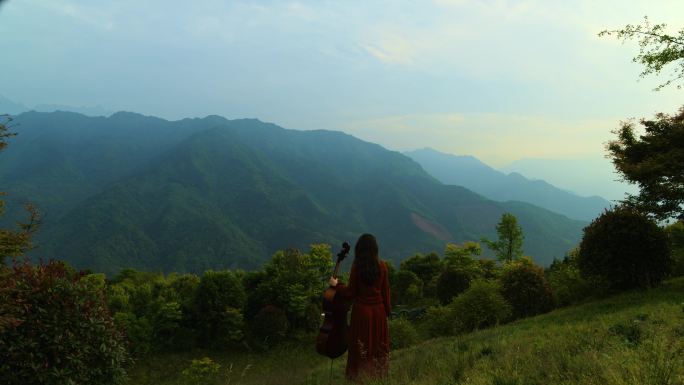 森林山坡上红衣女孩手扶大提琴航拍