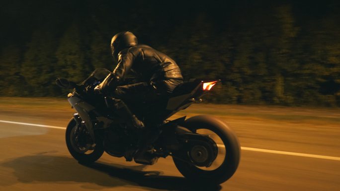年轻人骑着现代黑色运动摩托车在夜市街上