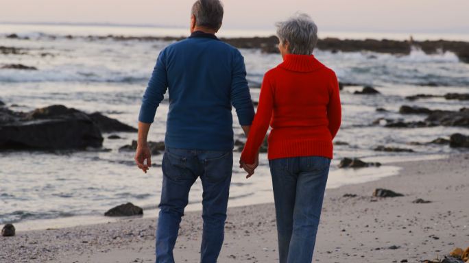 一对老夫妇手拉手在海滩上散步