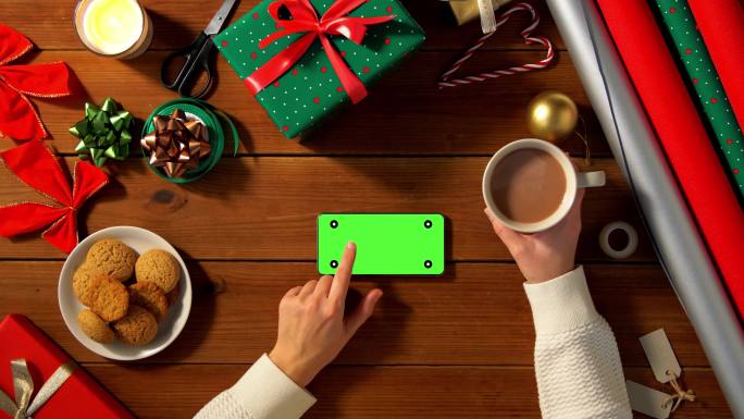 圣诞节使用绿屏智能手机和喝咖啡的女人