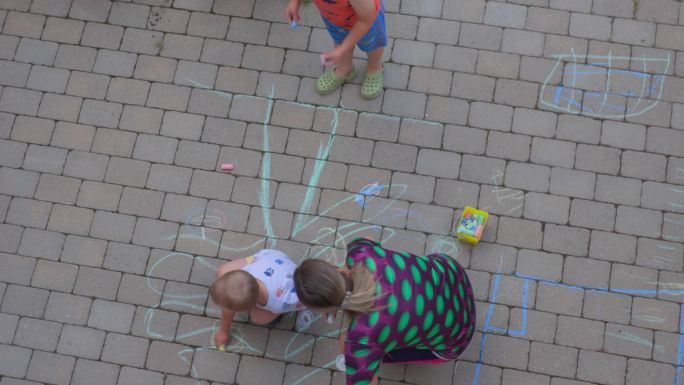 两个男孩和女人用彩色粉笔在铺路砖上画画