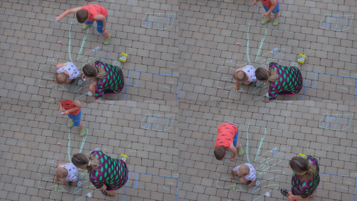 两个男孩和女人用彩色粉笔在铺路砖上画画