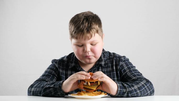 年轻的胖男孩吃了一个大汉堡