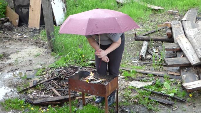 雨天，女人拿着雨伞在烤肉架上生火