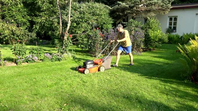 在自家院子里推着割草机的男人