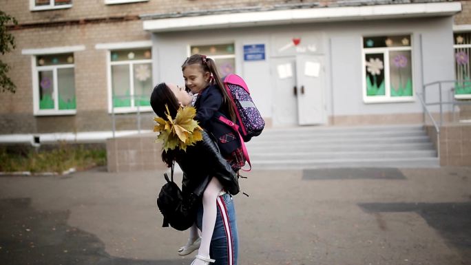 小女孩从学校跑出来迎接他的妈妈并拥抱她。
