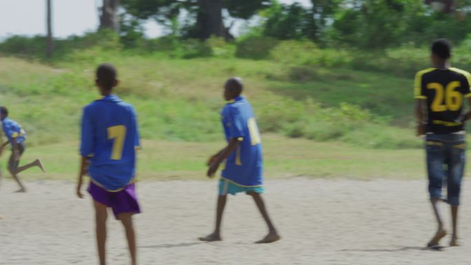 非洲男孩在沙地足球场踢足球
