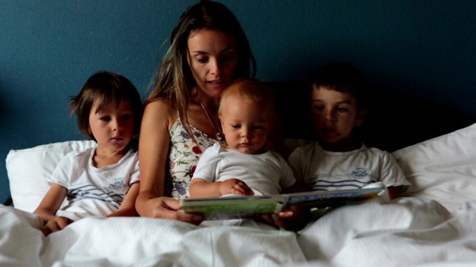 妈妈早上在家里的床上给孩子们读书