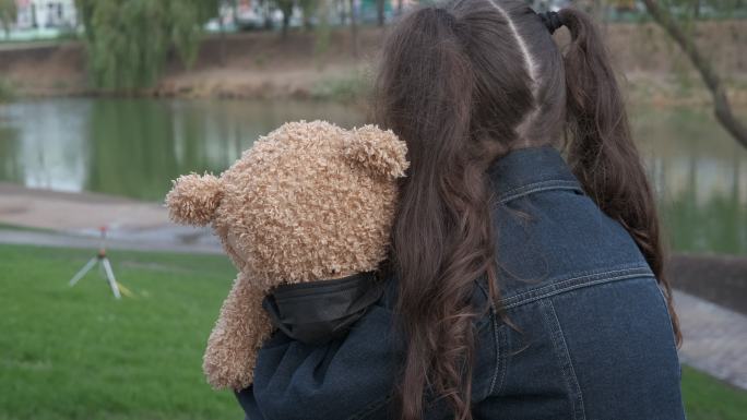 公园里，小女孩抱着一只小熊坐着。