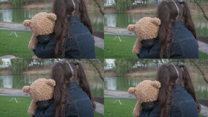 公园里，小女孩抱着一只小熊坐着。